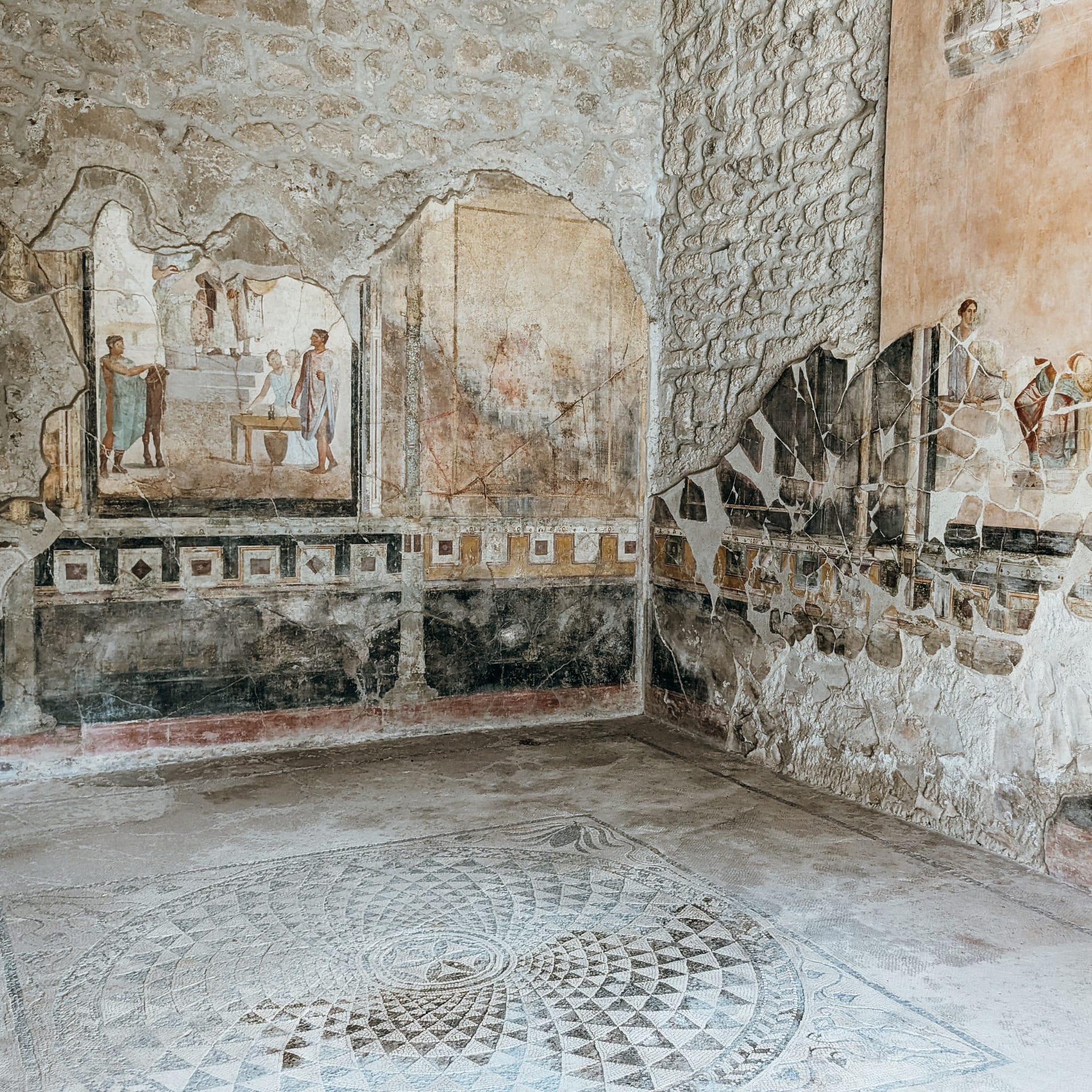 2 Ancient frescoes and mosaic floor in a partially ruined room with stone walls, depicting people and geometric patterns.
